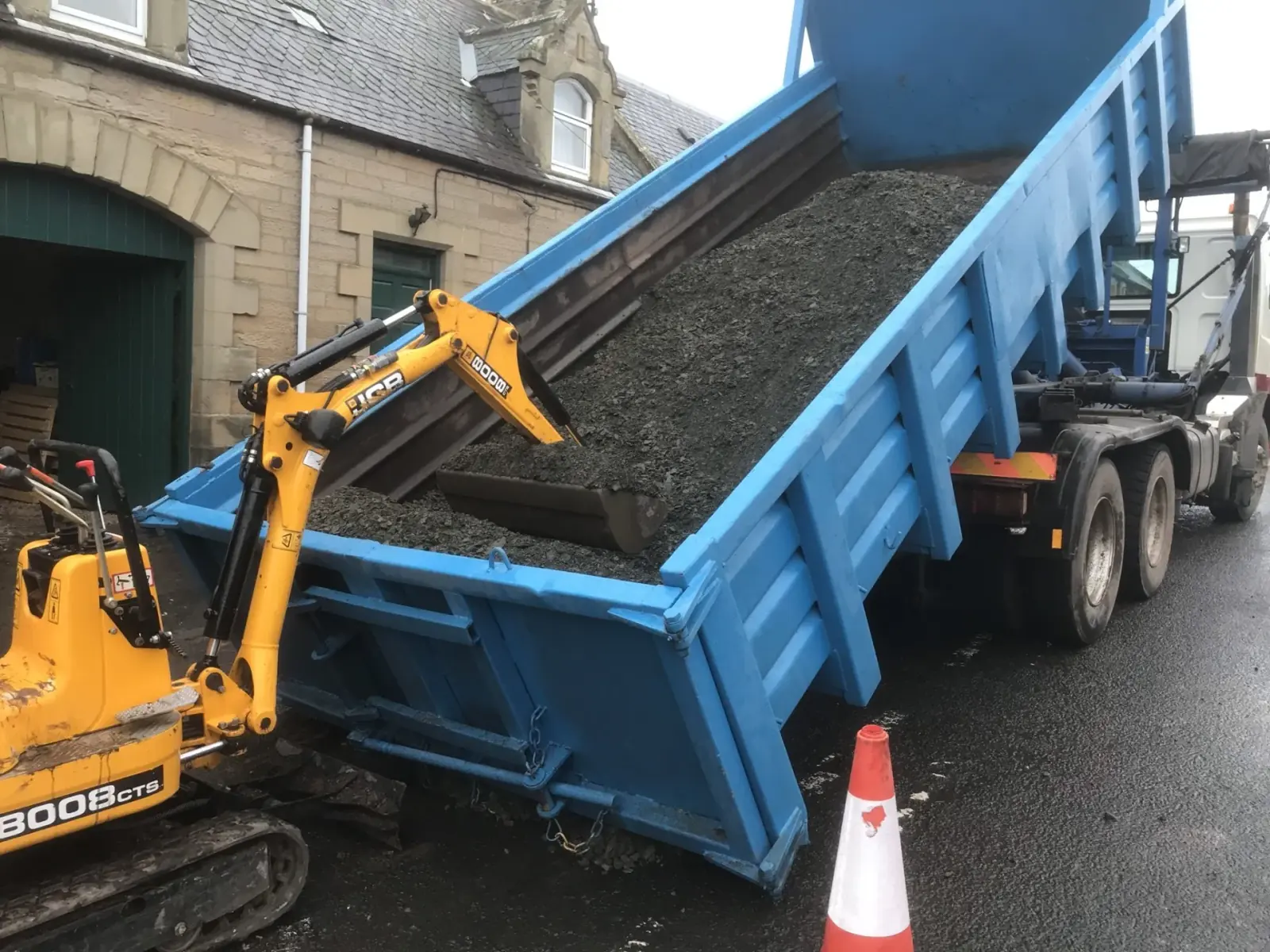 Tarmac being tipped from a lorry into a B&K Hume dumper on a village street job